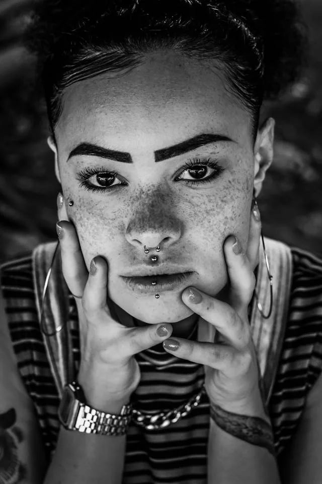 Schwarz-Weiß-Aufnahme eines Models mit Nasen- und Lippenpiercings sowie Creolen.